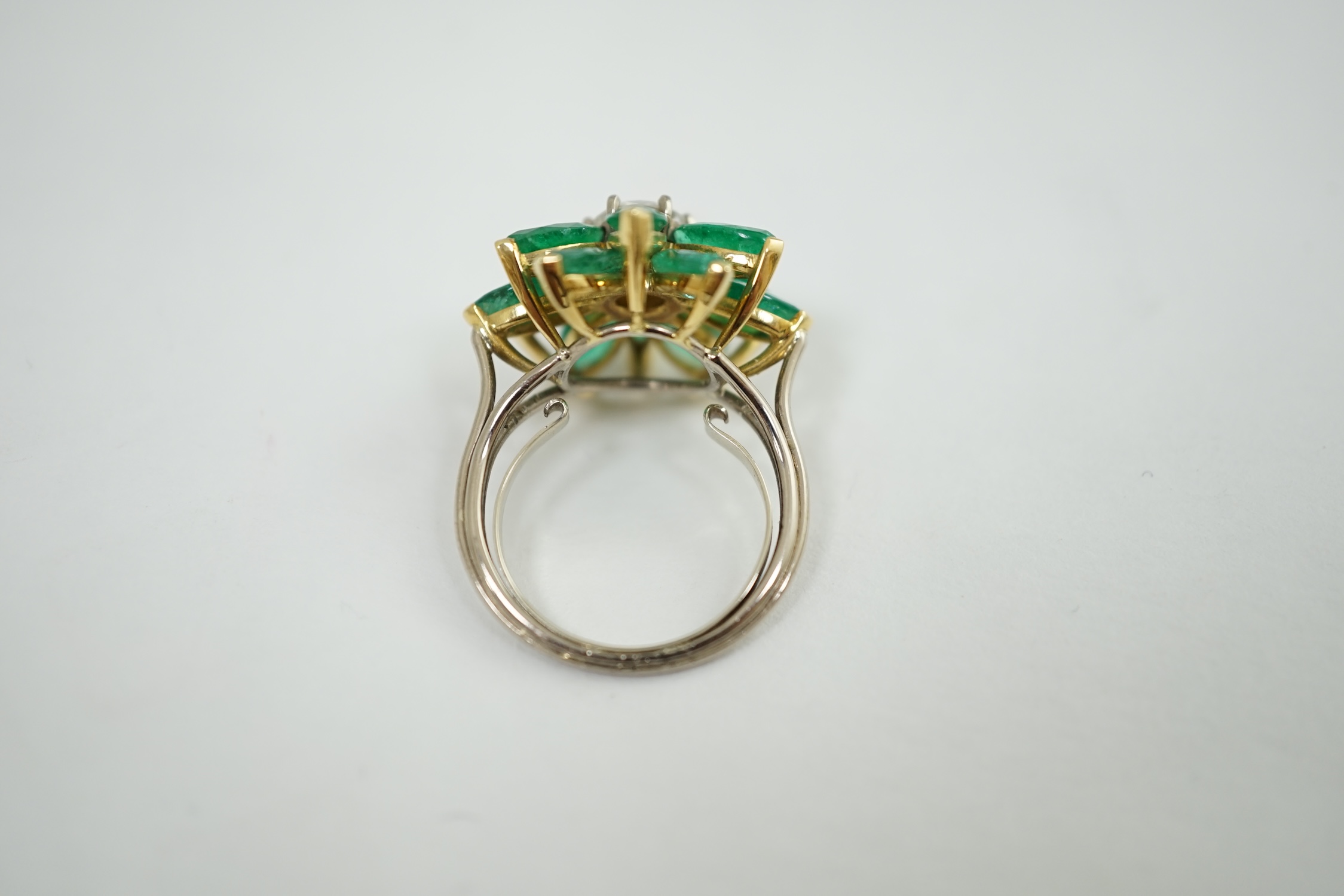 An 18ct white gold and yellow gold, emerald and diamond flowerhead dress ring, the central circular cut diamond surrounded by eleven navette shaped emerald 'petals', all claw set